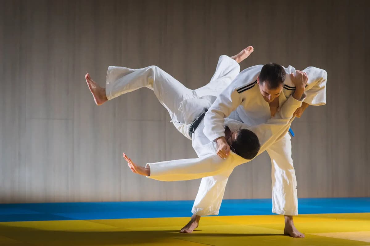 Twee judoka's in een witte judogi tijdens een worp op de mat